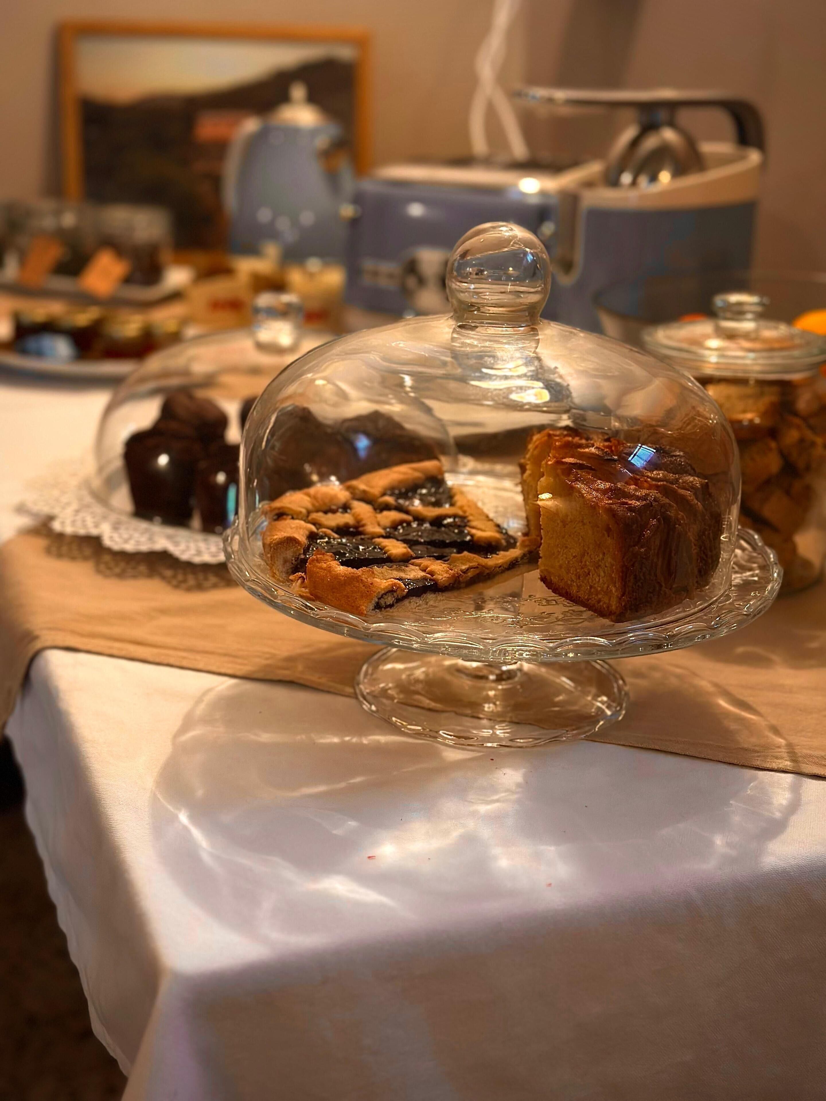 Een dessertpresentatie met een glazen koepel, een taart en een gebakken taart op een tafel.