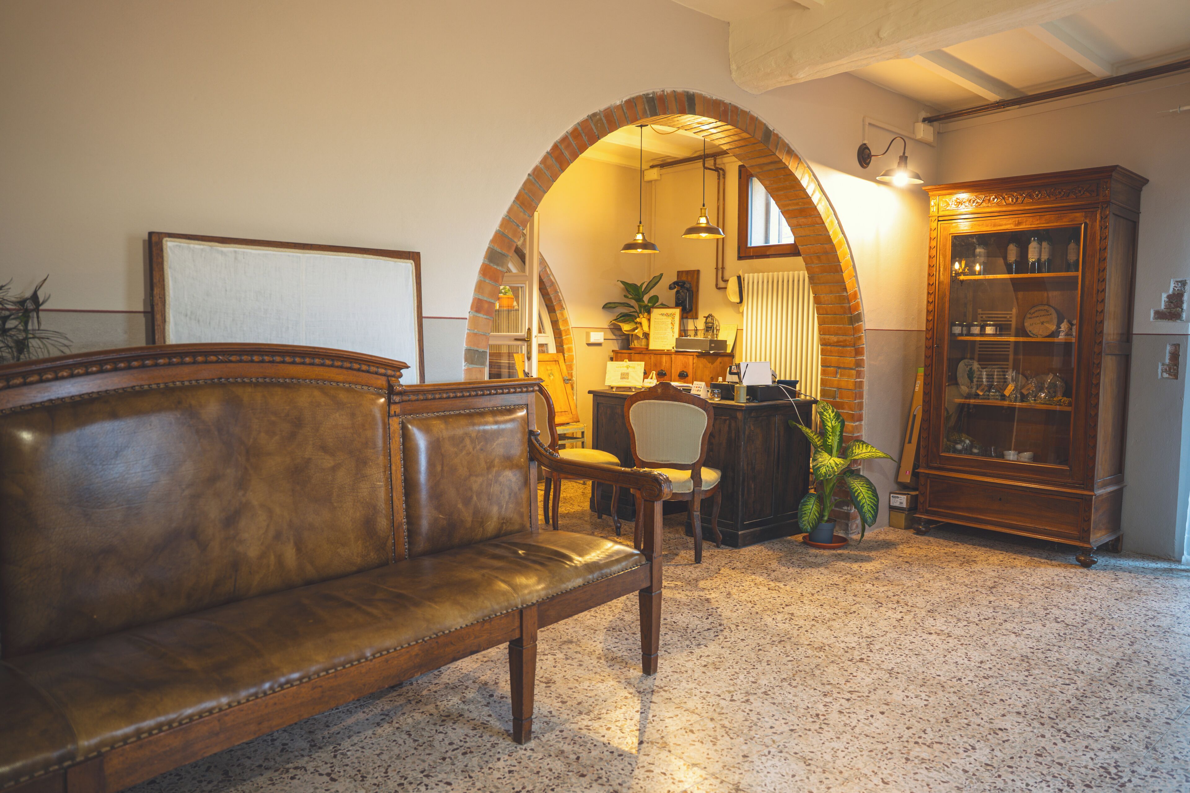 A cozy living room with a leather sofa, a wooden cabinet, and a brick archway leading to a kitchen area.