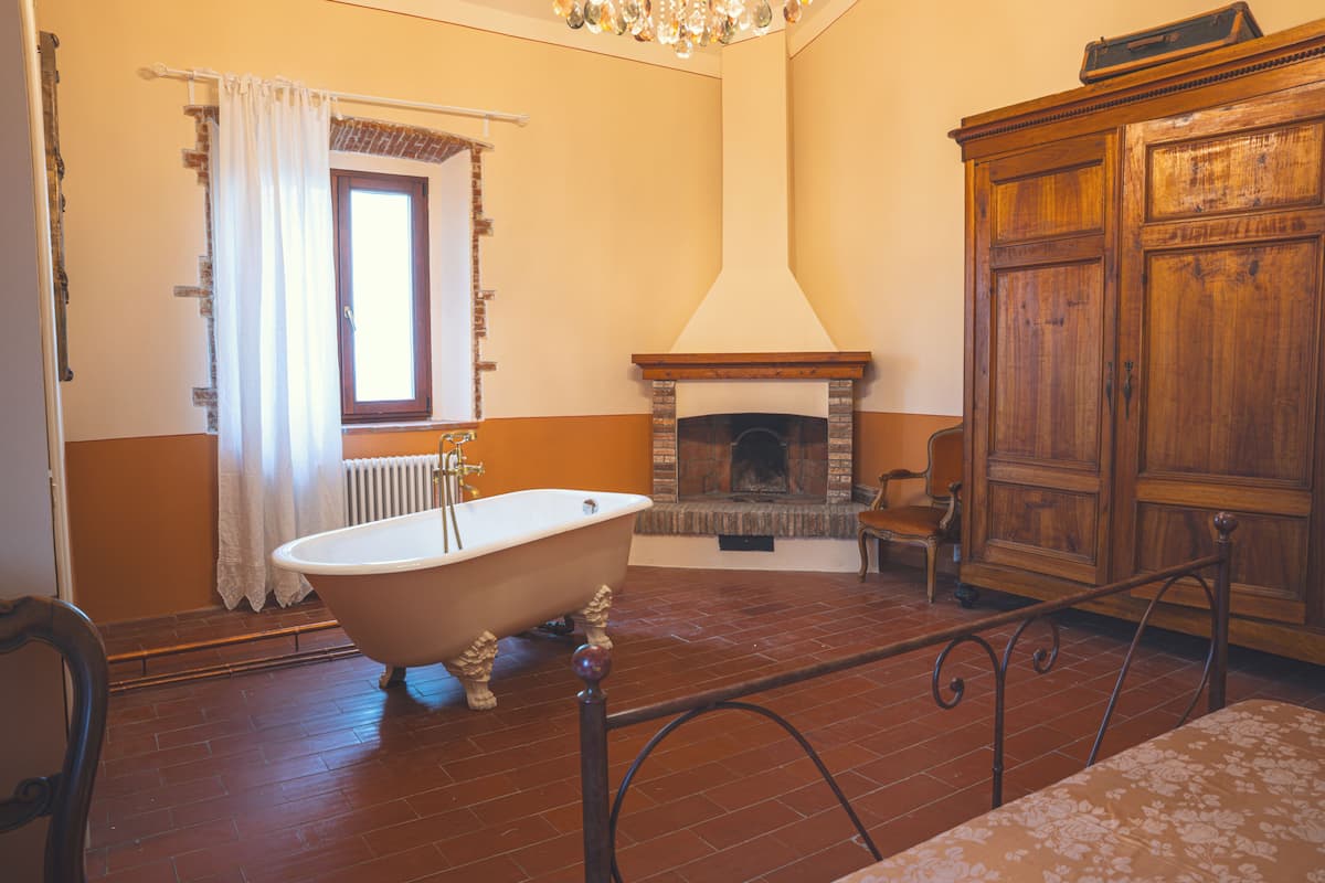 Una habitación con una bañera de patas de león, chimenea y un armario de madera.