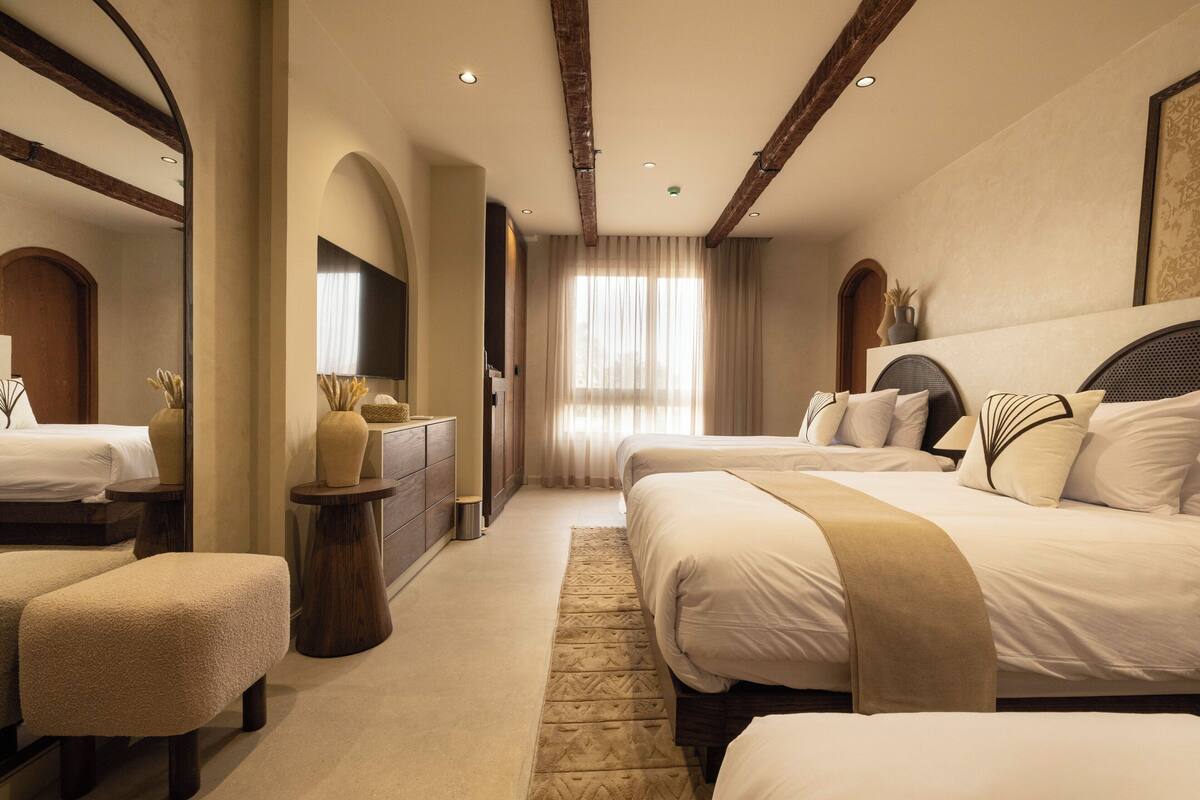 A hotel room with a large bed, a smaller bed, a desk, and a seating area.