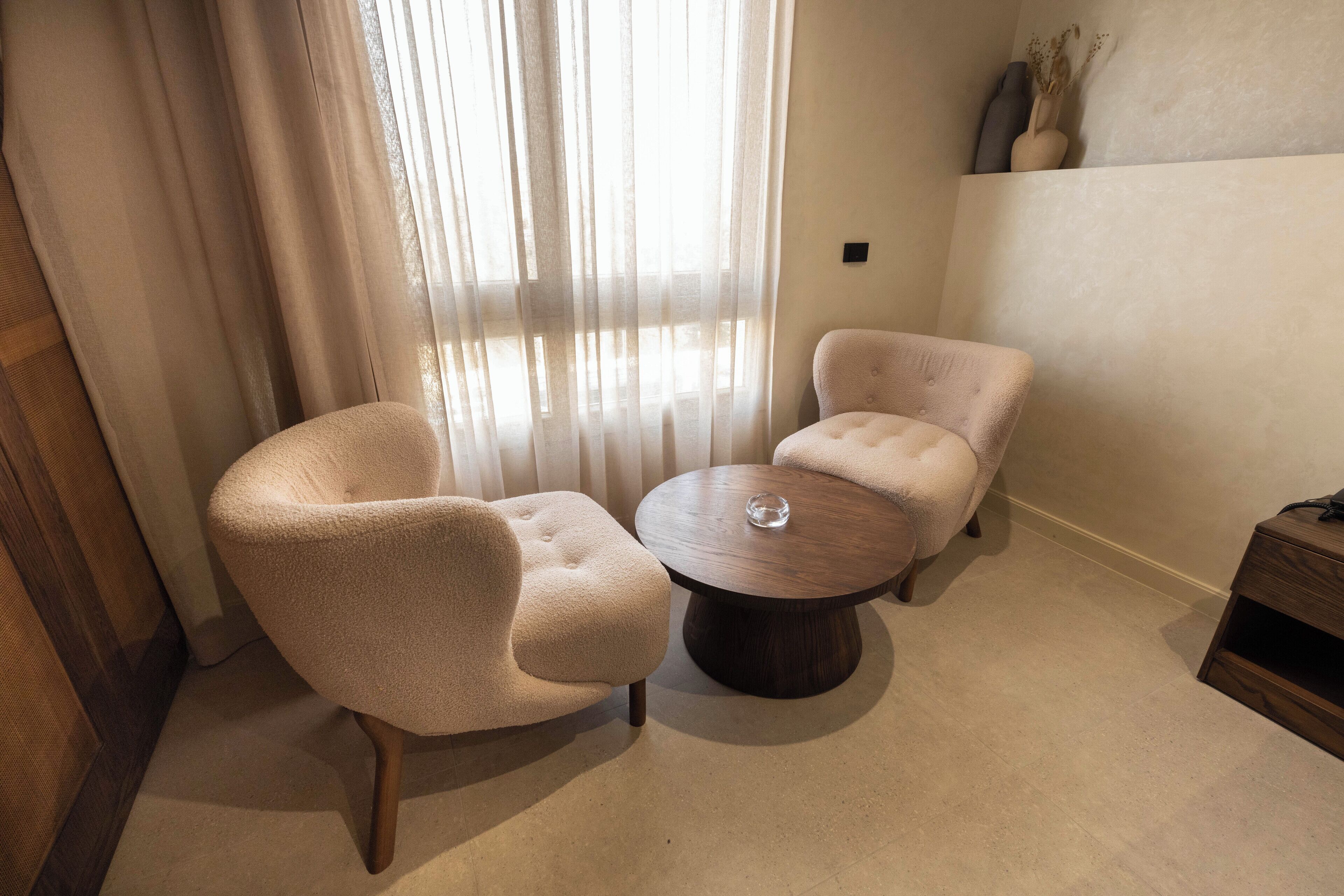 A room with two beige armchairs and a round wooden coffee table.