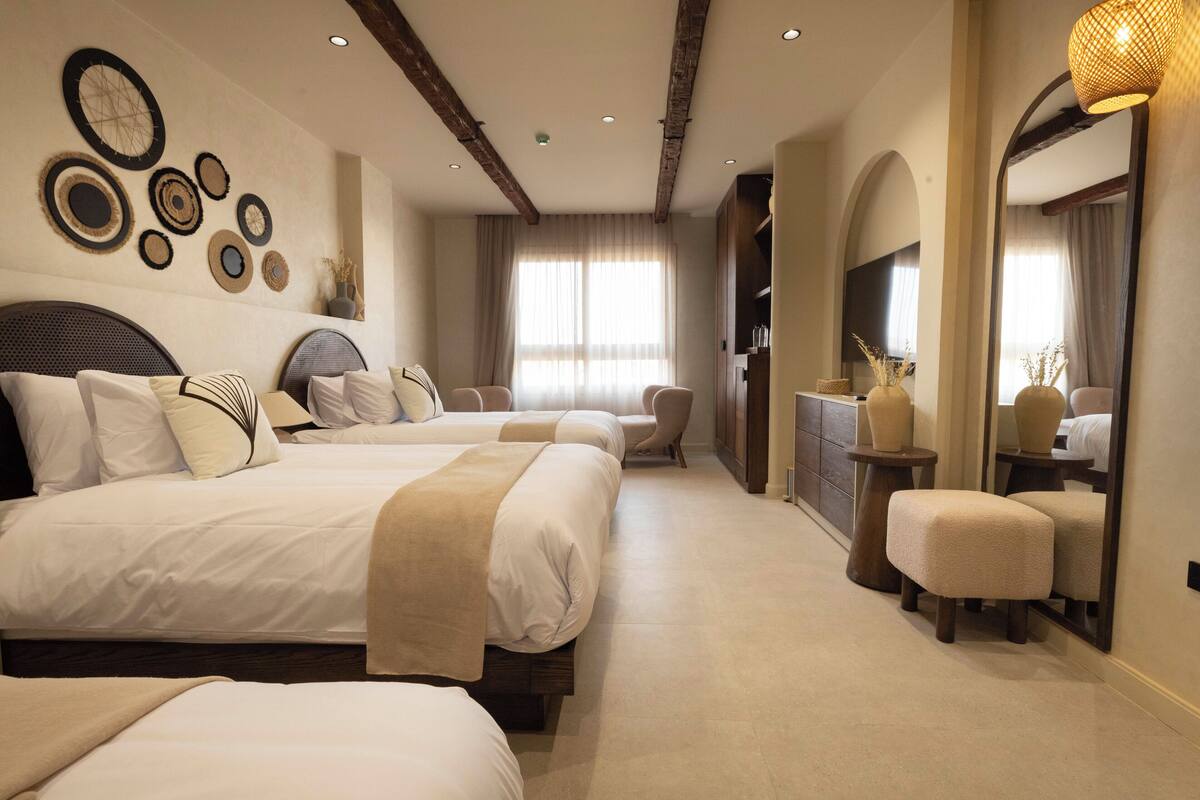 A spacious bedroom with three beds, a large mirror, and a wooden ceiling.
