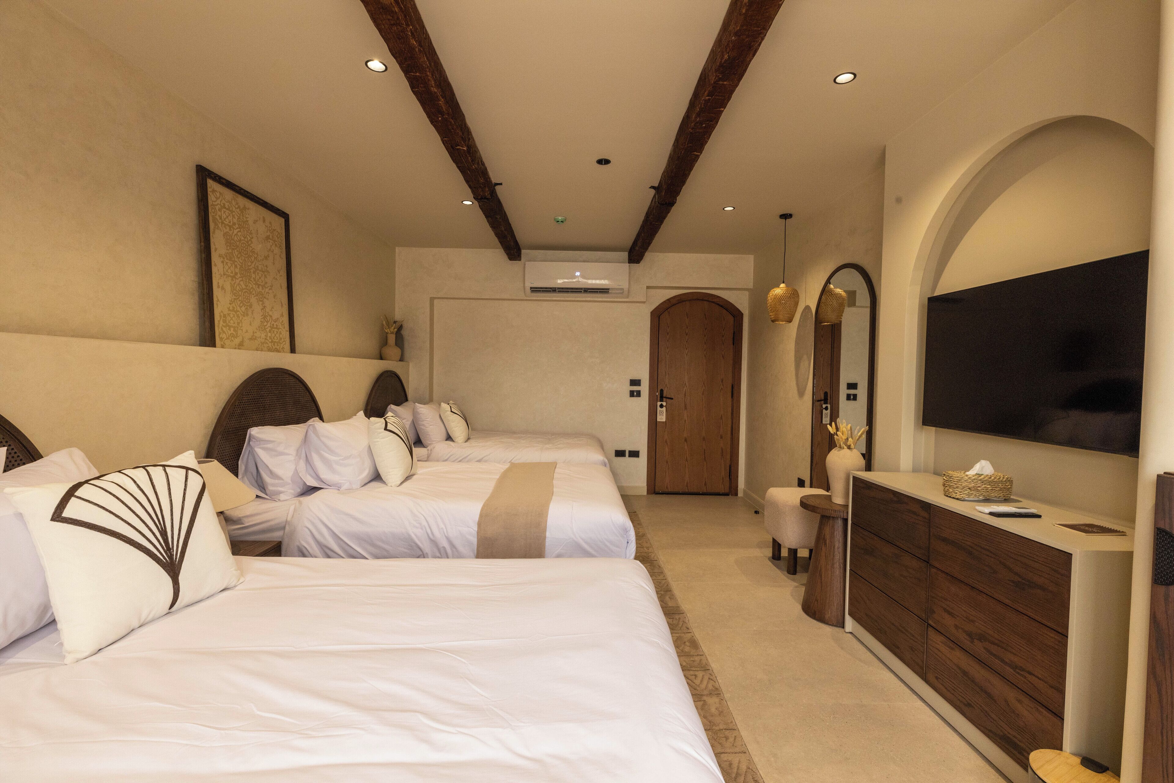 Une chambre d’hôtel avec deux lits, un plafond en bois, un grand miroir et un téléviseur fixé au mur.