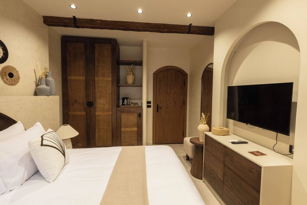 A bedroom with a bed, a TV, a dresser, and a wooden wardrobe.
