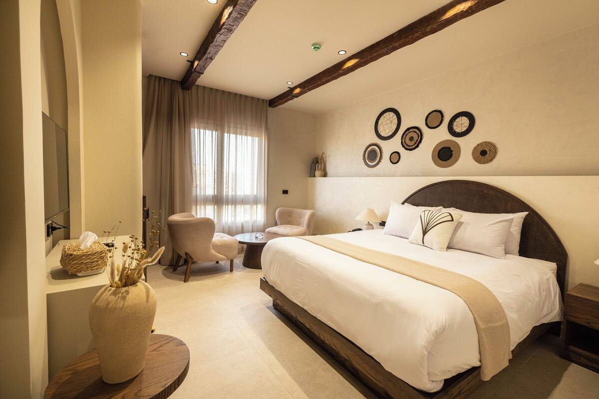 A hotel room with a large bed, two armchairs, a small table, and a decorative wall.