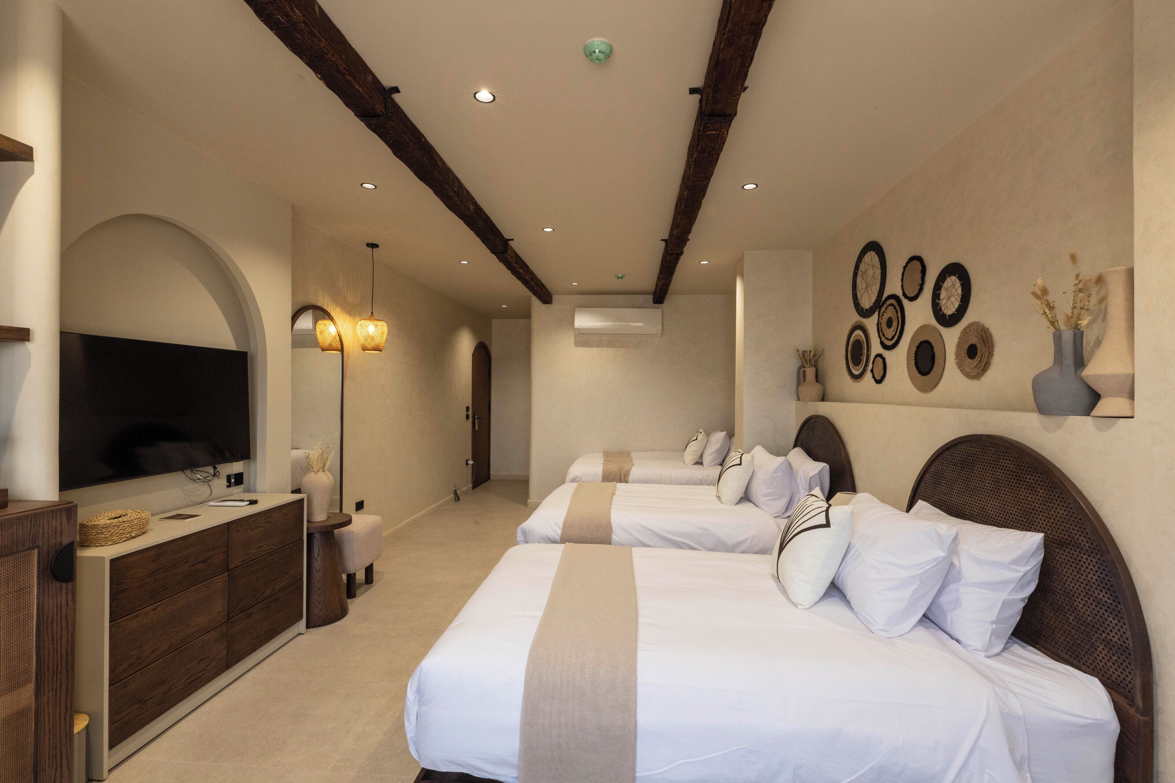 A hotel room with two beds, a TV, a dresser, and a wall with decorative plates.