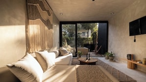 A modern living room with a sofa, a coffee table, and a TV mounted on the wall. There is a large window providing a view of the outside. - Paradise Villa, 3 Pools, Rooftop, VIP Concierge (Tulum)