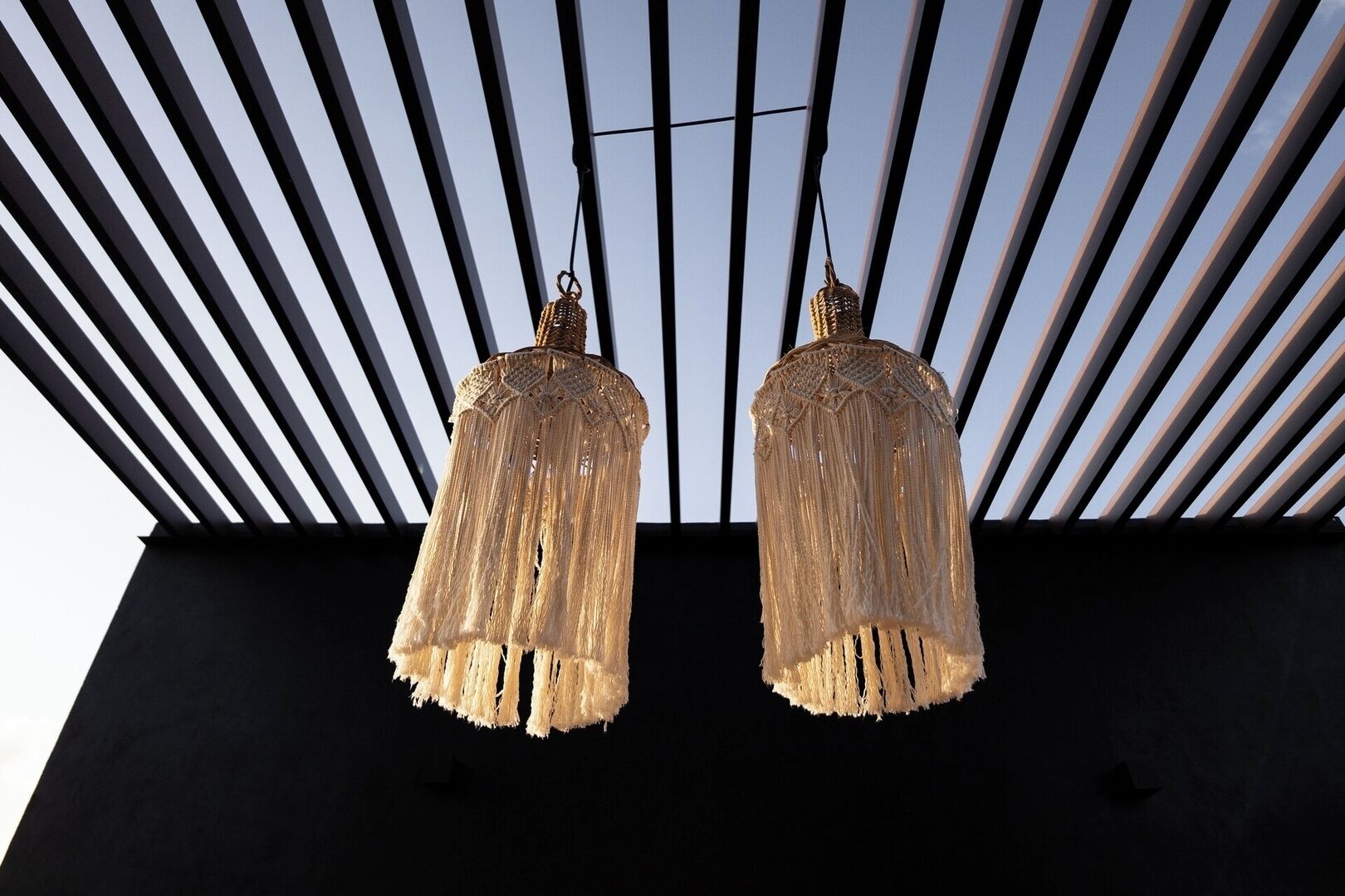 Two hanging chandeliers with fringed designs against a modern architectural backdrop with vertical lines.
