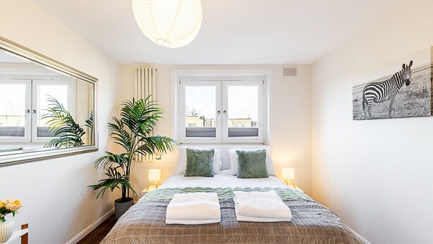 Una habitación de hotel con una cama grande, dos mesitas de noche, una planta en maceta, una ventana con vistas y un cuadro de cebra en la pared.