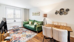 Una sala de estar con un sofá verde, una mesa de comedor de madera y una alfombra estampada.