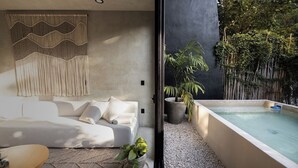Et moderne soveværelse med en stor seng, et lille bord og udsigt til et privat udendørs område med jacuzzi og planter.