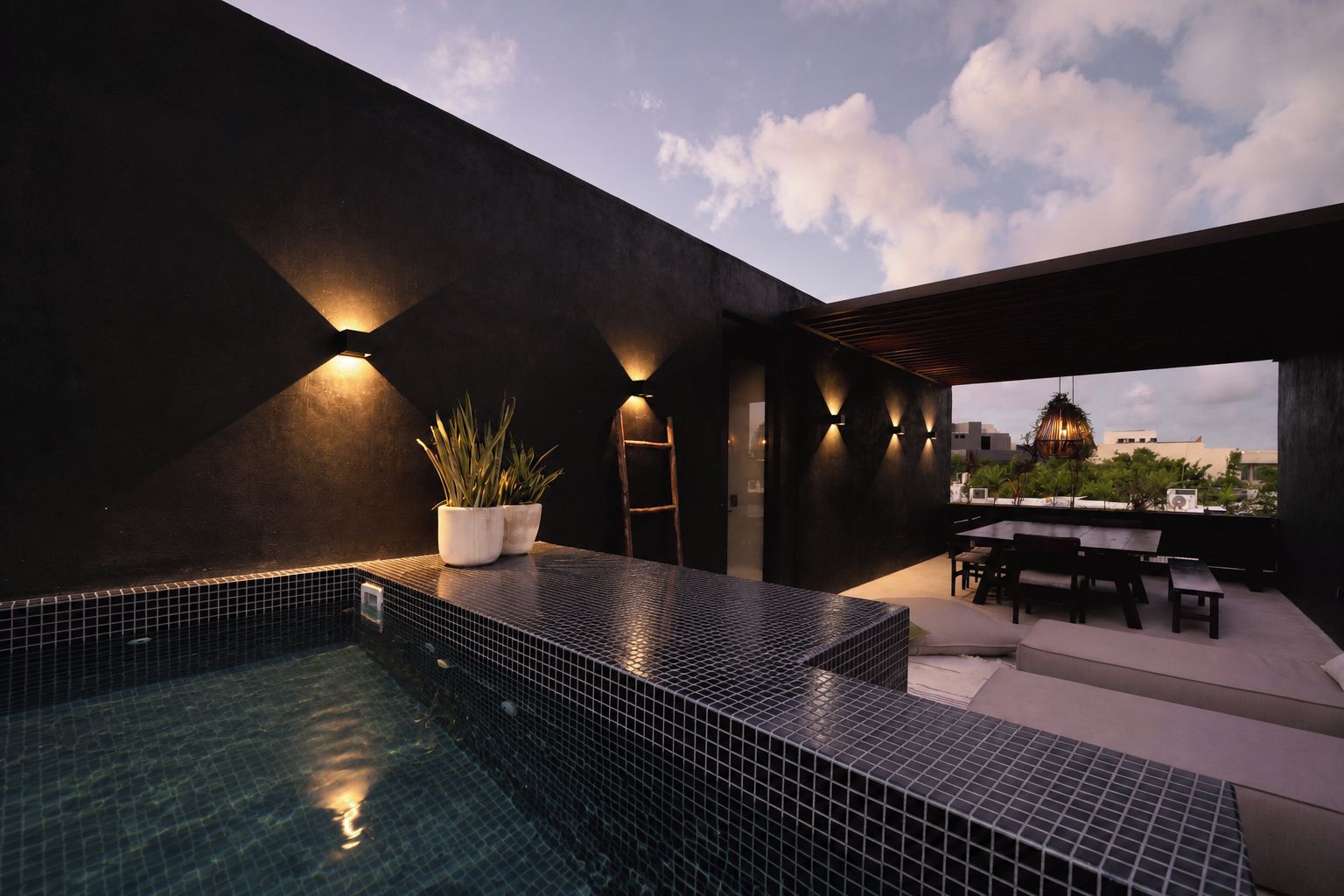A rooftop pool area with a tiled floor, a seating area with a table and chairs, and a view of the cityscape.