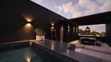 A rooftop pool area with a tiled floor, a seating area with a table and chairs, and a view of the cityscape.