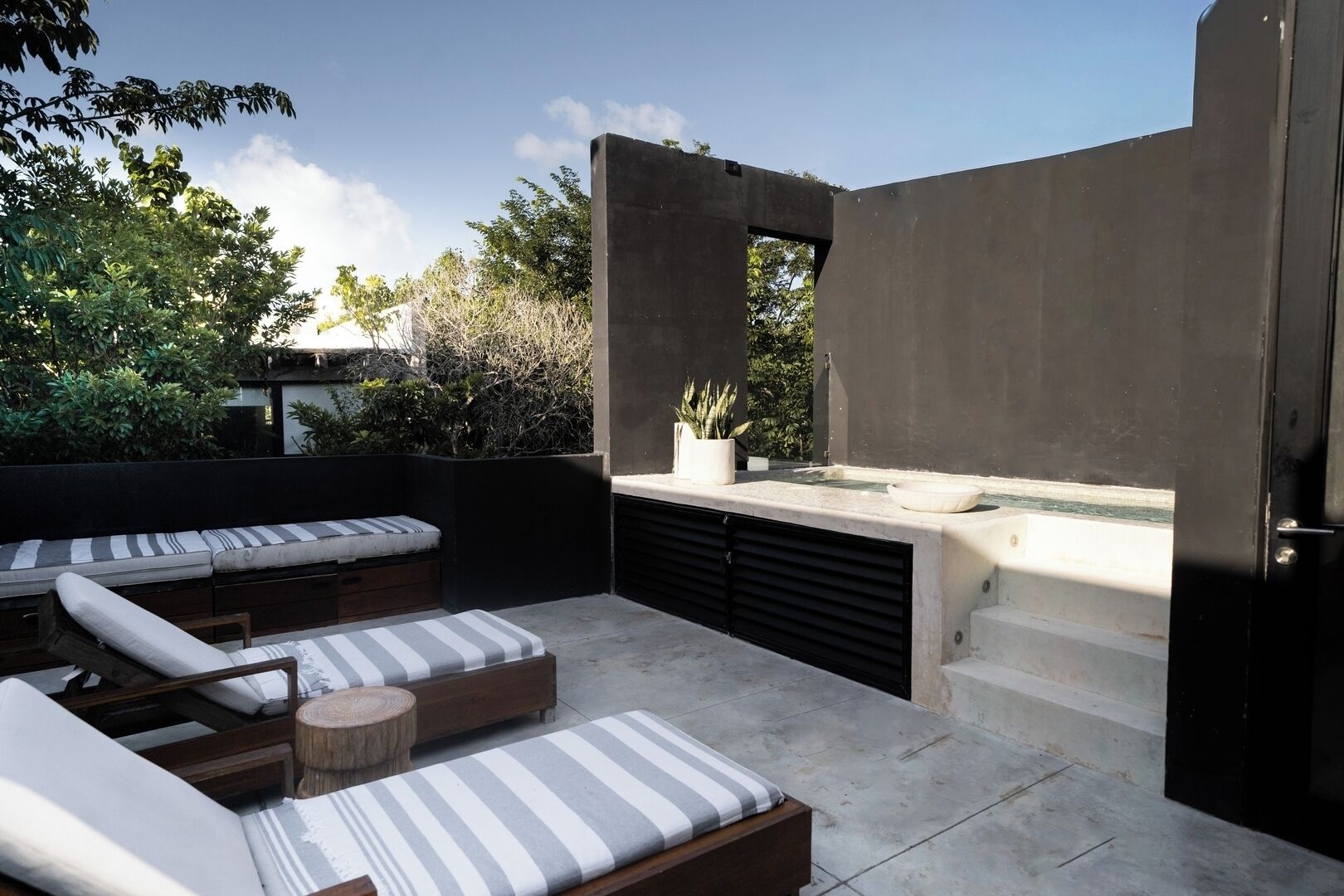 Een modern terras buiten met een ingebouwde jacuzzi, beklede zitplaatsen en een minimalistisch ontwerp.