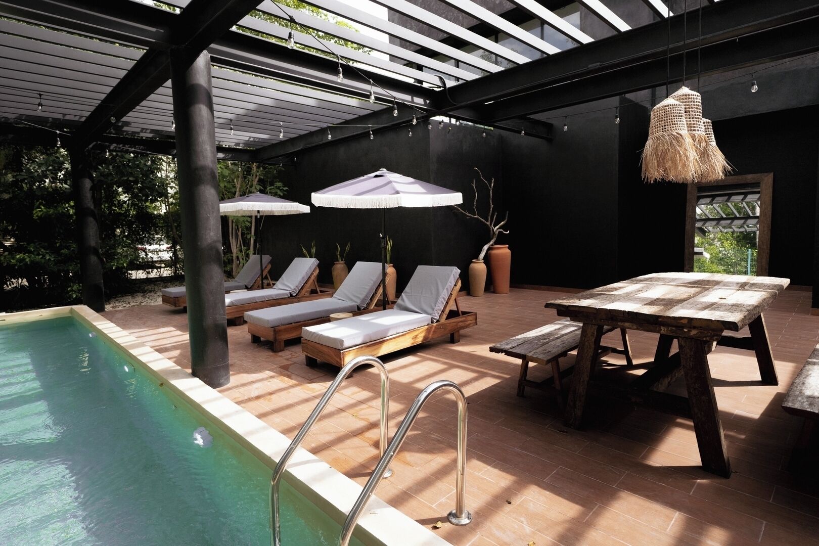 A poolside area with lounge chairs, a wooden table, and a hanging light fixture.