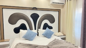 A hotel room with a large bed, a headboard with a decorative design, an air conditioning unit, a bedside table, and a curtain.