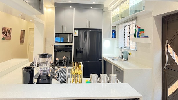 A modern kitchen with a built-in microwave, oven, and black refrigerator. There is a countertop with a blender, knives, and salt shakers.