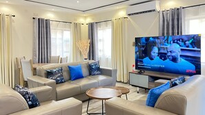 A modern living room with a leather sofa, a coffee table, and a flat-screen TV displaying a series.