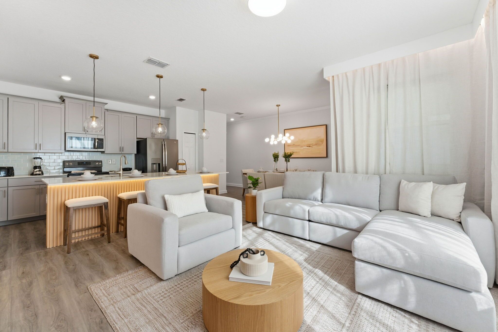 A modern living room with a large L-shaped sofa, a round coffee table, and a kitchen area with a bar.