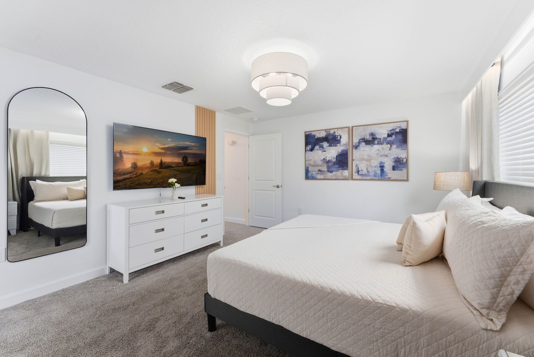A bedroom with a bed, a dresser, a mirror, and artwork on the walls.