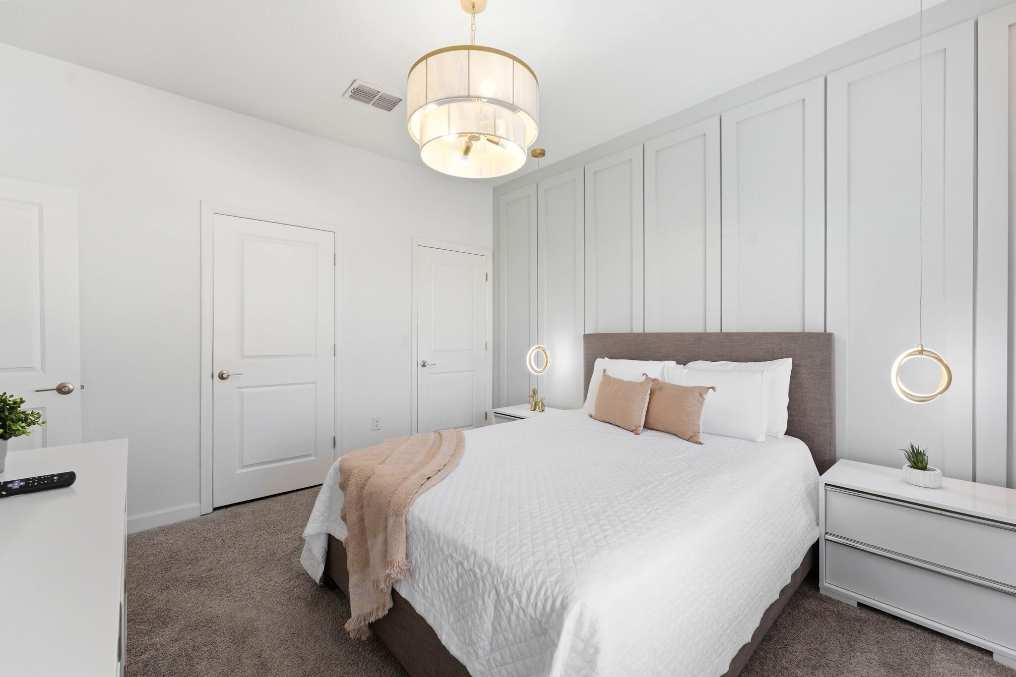 A bedroom with a large bed, bedside tables, a nightstand, a hanging light fixture, and a door.