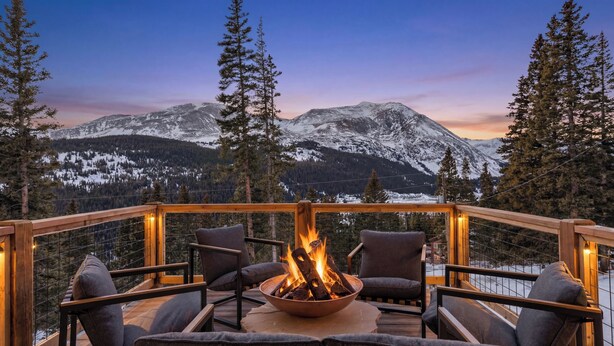 Una terraza con un pozo de fuego, sillas y vistas a montañas nevadas.