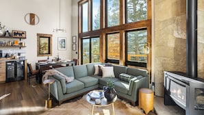 Un espacio de sala cómodo con un sofá modular, una chimenea y ventanas amplias con vista a árboles.