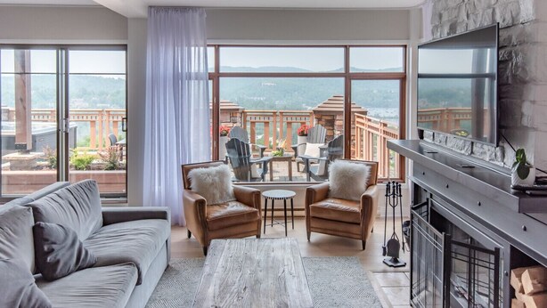 A spacious living room with a large window, a fireplace, and a balcony with outdoor furniture. - Altitude Ski-in/Out at Resort with Private Hottub (Mont-Tremblant)
