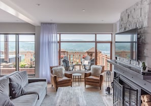A spacious living room with a large window, a fireplace, and a balcony with outdoor furniture. - Altitude Ski-in/Out at Resort with Private Hottub (Mont-Tremblant)