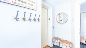 A hallway with a welcome sign, coat hooks, a mirror, and wooden stools. - Altitude Ski-in/Out at Resort with Private Hottub (Mont-Tremblant)