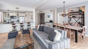 A modern open-plan living area with a grey sofa, wooden dining table, and bar stools. - Altitude Ski-in/Out at Resort with Private Hottub (Mont-Tremblant)