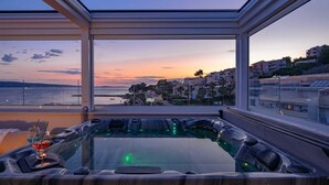 A modern spa area with a glass enclosure, a hot tub, and a view of a coastal town at sunset. - Beachfront Villa Lara with Pool (Duće)