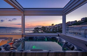 A modern spa area with a glass enclosure, a hot tub, and a view of a coastal town at sunset. - Beachfront Villa Lara with Pool (Duće)