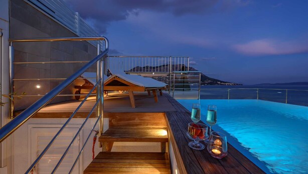 A poolside area with a wooden deck, a lounge chair, and a glass table with drinks. - Beachfront Villa Lara with Pool (Duće)