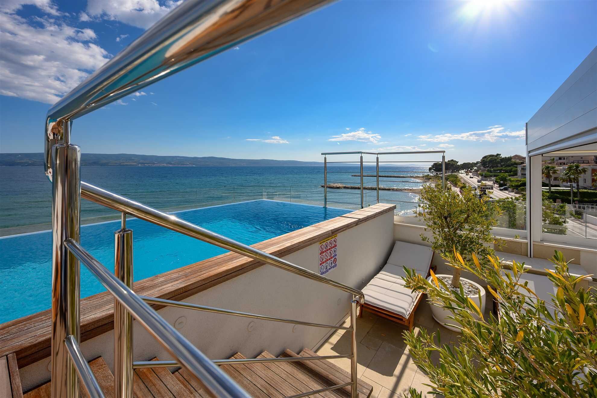 Ein Poolbereich mit Meerblick, eine Holzterrasse und eine Liege.