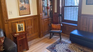 Een kamer met houten lambrisering, een boekenkast, een stoel, een vloerkleed en een raam met uitzicht.