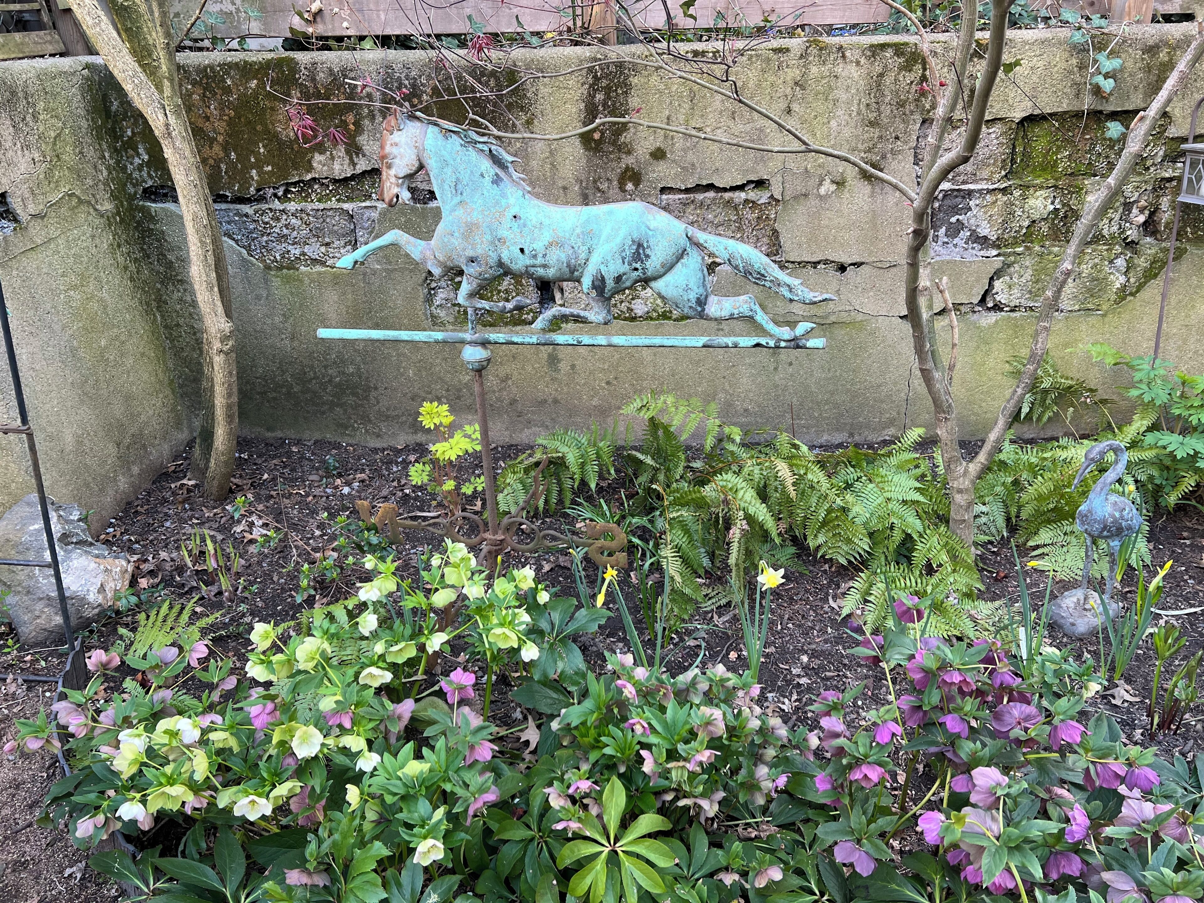 A garden with a bronze horse sculpture, ferns, and flowering plants.