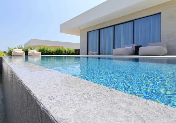 A modern pool area with a clear blue pool, lounge chairs, and a large sliding glass door.