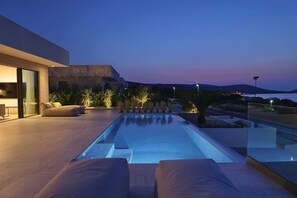 A modern outdoor pool area with a minimalist design, including a seating area with cushions and a clear view of the surrounding landscape.