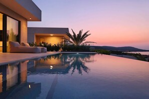 A modern infinity pool with a view of the sunset and mountains.