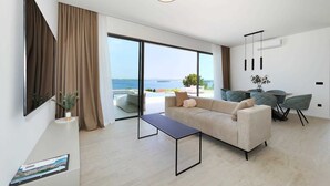 A modern living room with a sofa, a coffee table, and a dining area with chairs and a table. There is a large window providing a view of the sea. - Luxury Villa Pasman Aquamarine with Pool (Tkon)