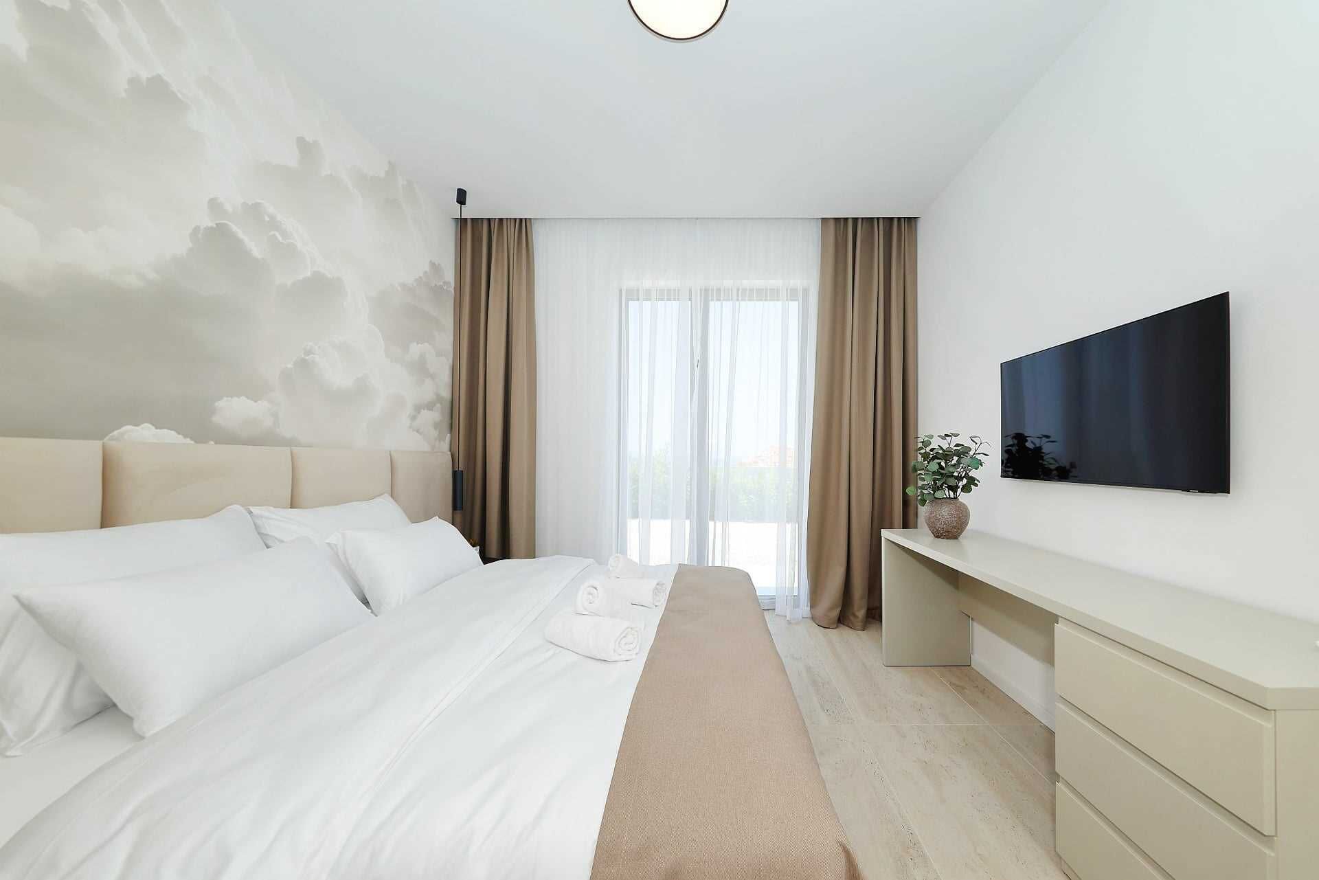 A modern bedroom with a bed, a TV, and a window with curtains.