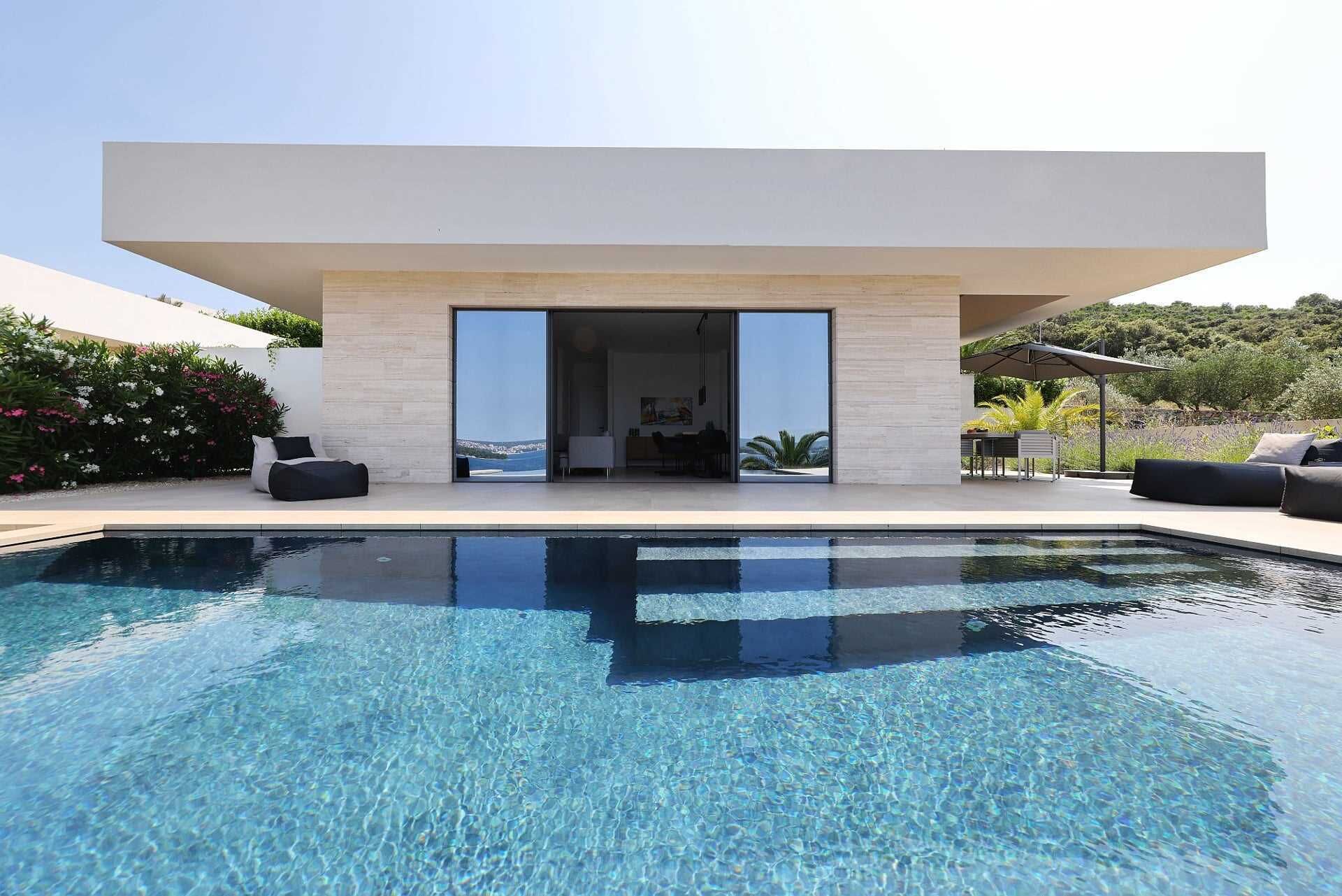 A modern house with a swimming pool, large glass doors, and outdoor furniture.