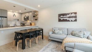 A modern kitchen with a dining area, a grey sofa, and a mountain landscape painting. - Avalanche Ridge (Revelstoke)