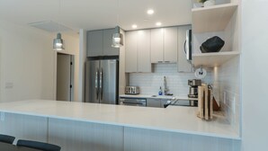A modern kitchen with a large island, stainless steel appliances, and pendant lighting. - Avalanche Ridge (Revelstoke)