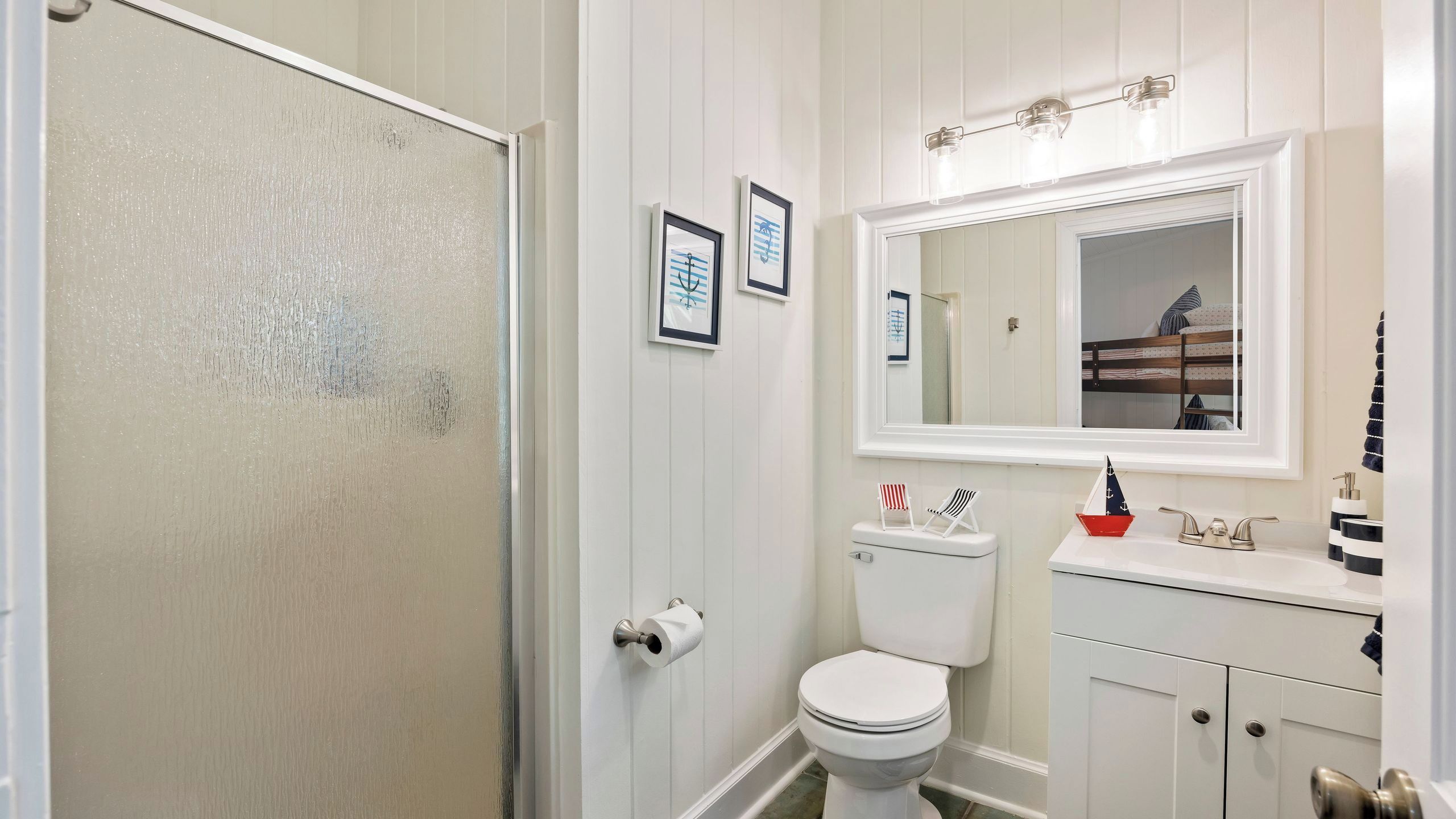 A bathroom with a toilet, sink, mirror, and framed artwork on the wall.