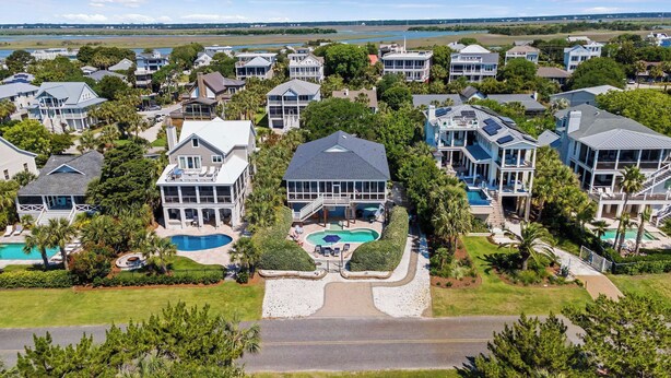A residential area with multiple houses, a central swimming pool, and a view of the water body in the background. - Historic Retreat Near Beach w/ Pool 306 Charleston Blvd Roosevelt Retreat by Avantstay (Isle of Palms)