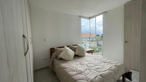 A bedroom with a bed, a window with a city view, a wardrobe, and a light switch on the wall. - Apartment 3 Bedrooms - Swimming Pool - City View (Armenia)