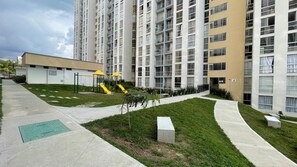 A modern apartment building with a playground, green lawns, and a clear sky. - Apartment 3 Bedrooms - Swimming Pool - City View (Armenia)