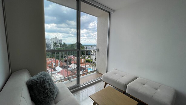 A modern apartment with a large balcony, white furniture, and a view of a residential area with buildings and a swimming pool. - Apartment 3 Bedrooms - Swimming Pool - City View (Armenia)